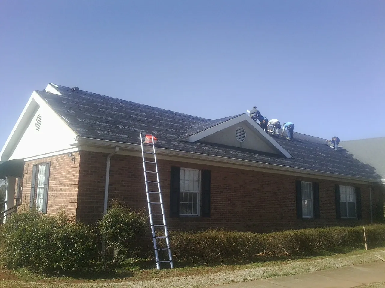 Crew tearing shingles off a brick ranch roof with a ladder set — Metal Roof Repair work by our crew in Simi Valley