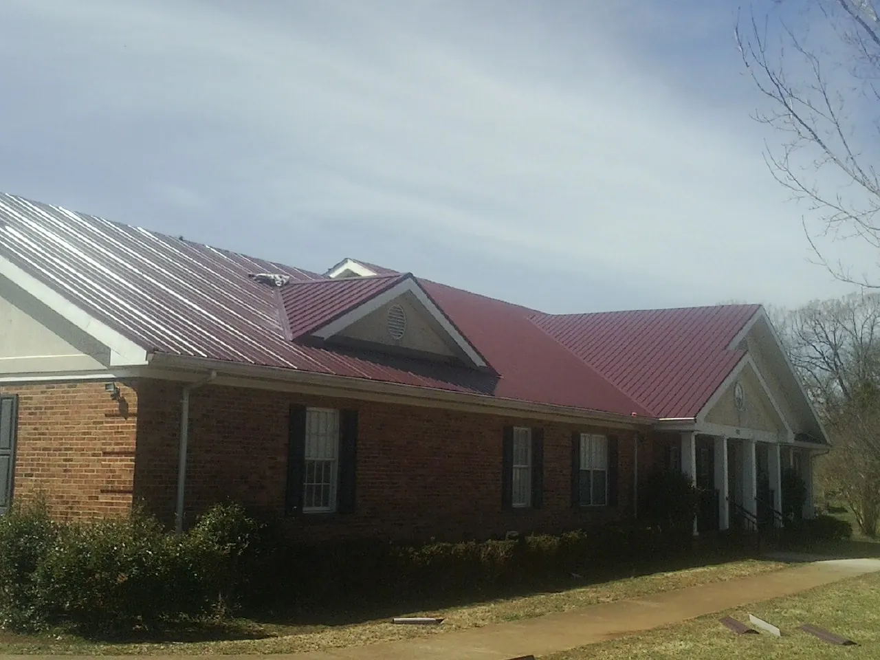 Red metal roof with gabled entries on a long brick building, from a Hail Damage Roof Repair job in Simi Valley