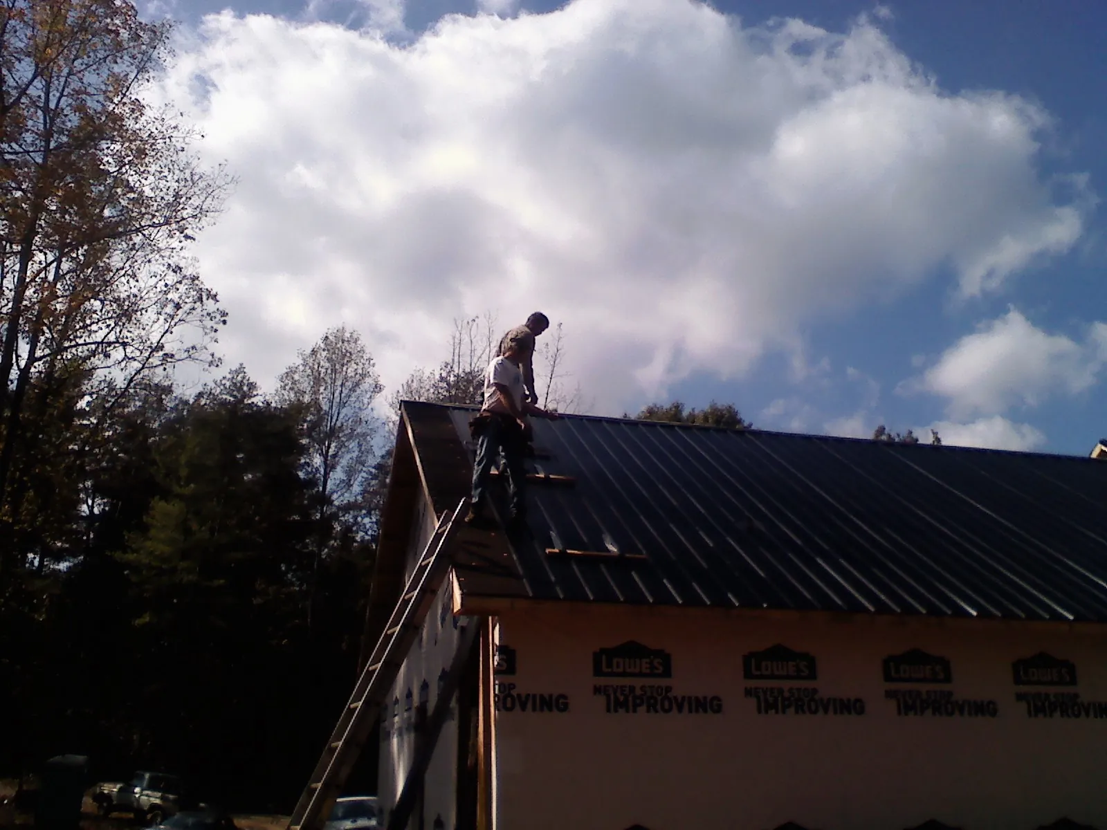 Roofer fastening dark metal panels high against a cloudy sky, from a Roof Inspection job in Simi Valley